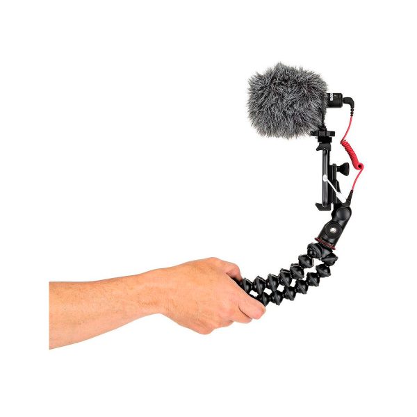 Käsi pitää JOBY GripTight PRO 2 GorillaPod Jalustakit Puhelimelle kameran ja ulkoisen mikrofonin (karvaisella tuulisuojalla) kanssa valkoista taustaa vasten.