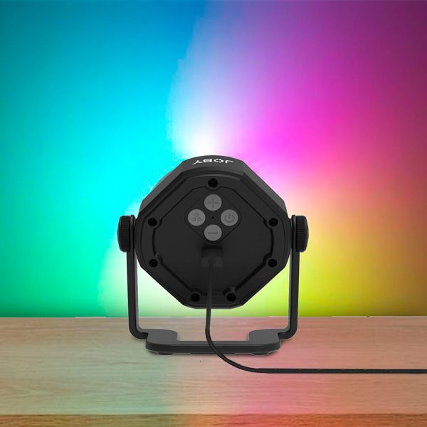 Joby Beamo Studio Background LED-valo istuu puupinnalla ja heijastaa sen takana olevalle seinälle sinisen, vihreän, vaaleanpunaisen ja keltaisen värisävyjä. Valosta lähtee virtajohto.