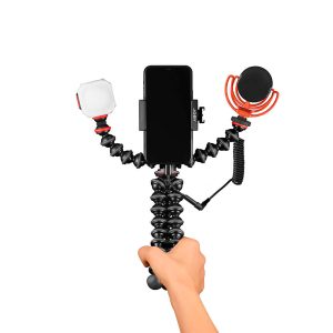 Käsi pitää Joby GorillaPod Advanced Mobile Vlogging Kit - jossa on asennettu älypuhelin, LED-valo vasemmalla ja ulkoinen mikrofoni punaisella iskukiinnikkeellä oikealla - valkoisella taustalla.