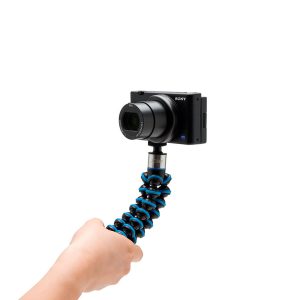 Käsi pitää kompaktia Sony-kameraa, joka on kiinnitetty Joby GorillaPod Go 500 + GripTight 360 Tripod Kit Blue -jalustaan, eristettynä valkoiselle taustalle.