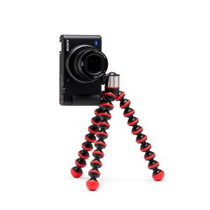 Joby-GorillaPod-Go-500-+-GripTight-360-Tripod-Kit-Red-2 Joby GorillaPod Go 500 + GripTight 360 Tripod Kit Red tukee mustaa digitaalikameraa, ja sen joustavat punaiset ja mustat segmenttijalat on sijoitettu valkoista taustaa vasten.