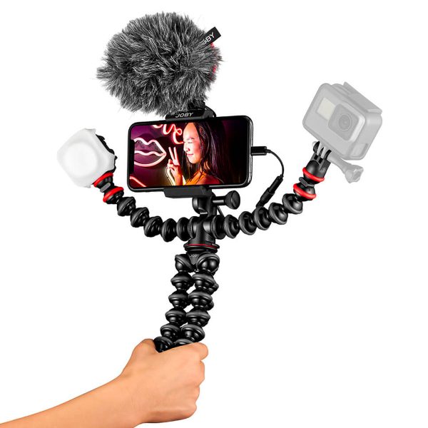 Kädessä on Joby GorillaPod Mobile Vlogging Kit, jossa on joustava kolmijalka, älypuhelimen kiinnike, mikrofoni, jossa on karvainen tuulisuoja, LED-valo ja toimintakamera - täydellinen mobiiliin videokuvaukseen tai vloggaamiseen.