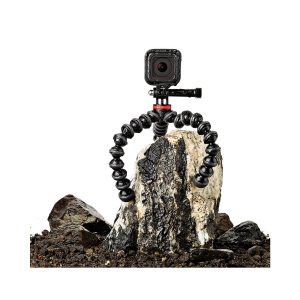 JOBY GorillaPod 500 Action Jalusta Musta/Harmaa, jonka joustavat jalat kietoutuvat tukevasti kiven ympärille, tukee kompaktia kameraa maaperän ja pienempien kivien keskellä.