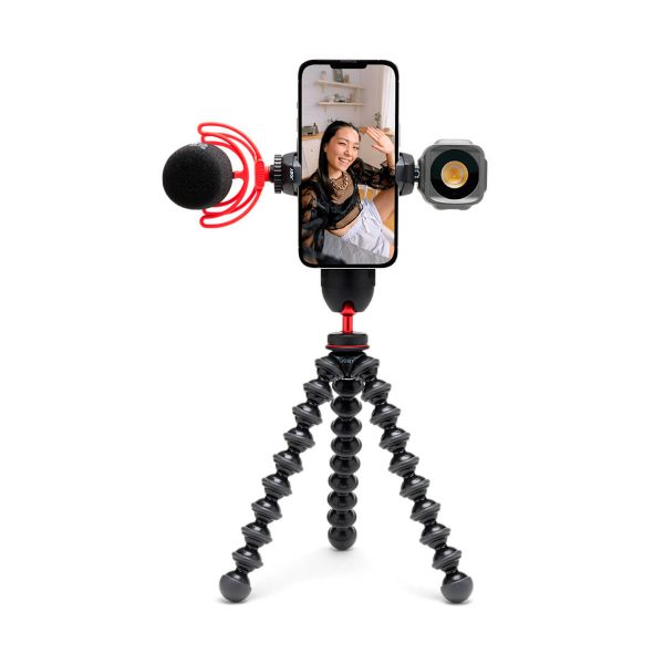 Joby-GripTight-Pro-3-kit-3 A woman smiles and flashes a smartphone screen attached to a Joby GripTight Pro 3 Kit phone stand with a microphone on the left and an LED light on the right on a flexible stand.