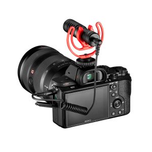 Musta Sony-digitaalikamera, jossa on suuri objektiivi ja jonka päälle on asennettu Joby Wavo Mobile - Mikrofoni kierrekaapelilla. Mikrofonissa on punainen iskukiinnike, ja kamera näkyy takaa.