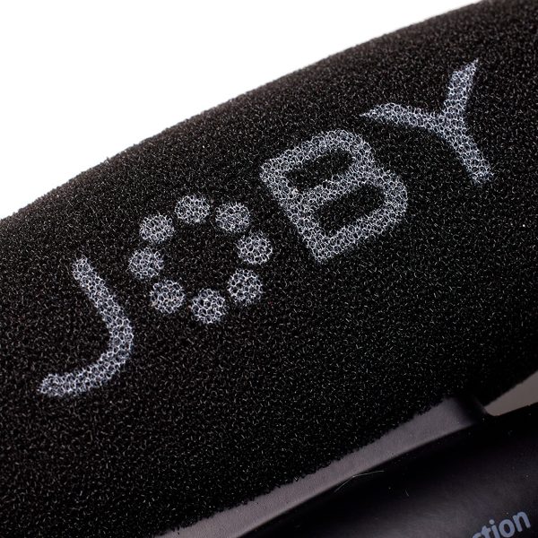 Lähikuva mustasta vaahtomuovisesta tuulisuojasta, jossa on valkoisilla kuvioiduilla kirjaimilla "JOBY", osa Joby Wavo Pro - Mikrofoni audio mikrofonin lisävarustetta.