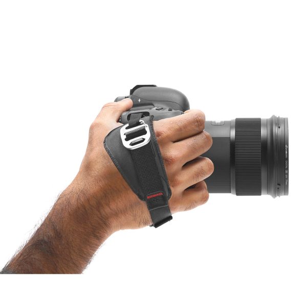 A person's hand holds the black DSLR camera with the Peak Design Clutch strap, which provides a secure grip when the camera lens is right-side up.