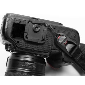 Close-up of the back and side of a DSLR camera with lens, quick release plate underneath and black Peak Design Clutch strap attached with an anchor link.