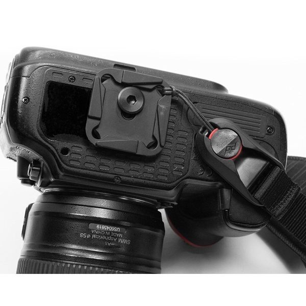 Close-up of the back and side of a DSLR camera with lens, quick release plate underneath and black Peak Design Clutch strap attached with an anchor link.