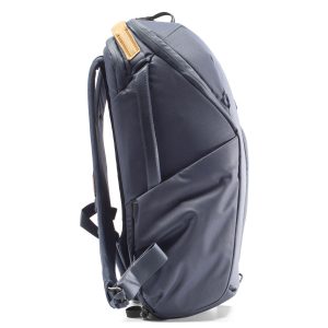 Peak Design Everyday Backpack Zip 20L -kamerareppu tummansinisessä sivukuvassa näkyy sen tyylikäs tummansininen muotoilu, useat lokerot, pehmustetut hihnat ja ruskehtavan sävyinen yläkahva. Reppu seisoo pystyssä valkoisella pohjalla.