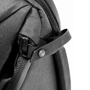 Lähikuva Peak Design Everyday Backpack v2 30L -kamerareppu, musta, jossa näkyy vetoketjun vetoketju, joka on kiinnitetty hihnaan, jossa on painonappi, ja jossa korostuu laukun tukeva musta kangas ja yksityiskohtainen muotoilu.