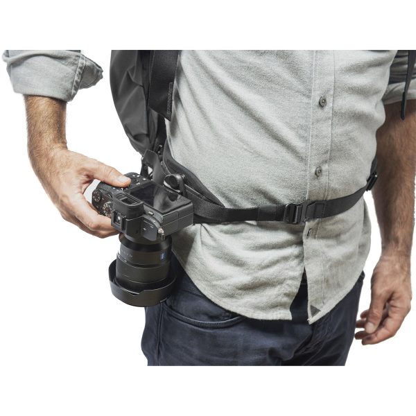 Henkilö, jolla on vaaleanharmaa paita ja reppu päällään, käyttää Peak Design Everyday Hip Belt V2 - Midnight (29-52") -vyötä ja pikakiinnikettä kiinnittääkseen kameransa turvallisesti sivulleen.
