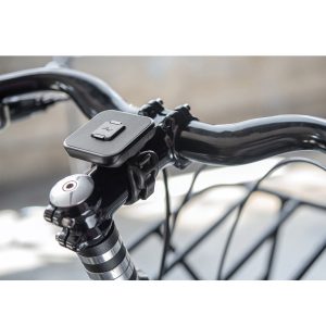 Lähikuva Peak Design Mobile Universal Bar Mount - musta kiinnitetty polkupyörän ohjaustankoon, jossa näkyy kaksi painiketta ja pieni LED-merkkivalo, ulkona sumealla taustalla.