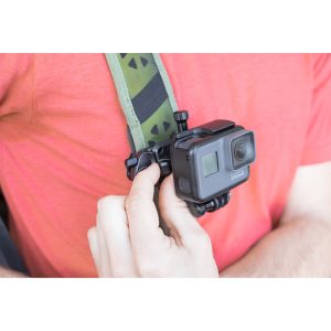 Henkilö säätää mustaa action-kameraa, joka on kiinnitetty hänen rintaansa Peak Design POV Kit for Capture -laitteella, jossa on vihreä ja musta kuvioitu hihna.
