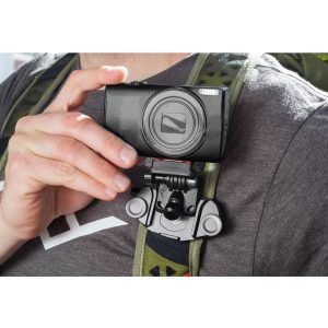 Harmaaseen paitaan ja reppuun pukeutunut henkilö pitää mustaa kameraa, joka on kiinnitetty reppuhihnaan Peak Design POV Kit for Capture -laitteella.