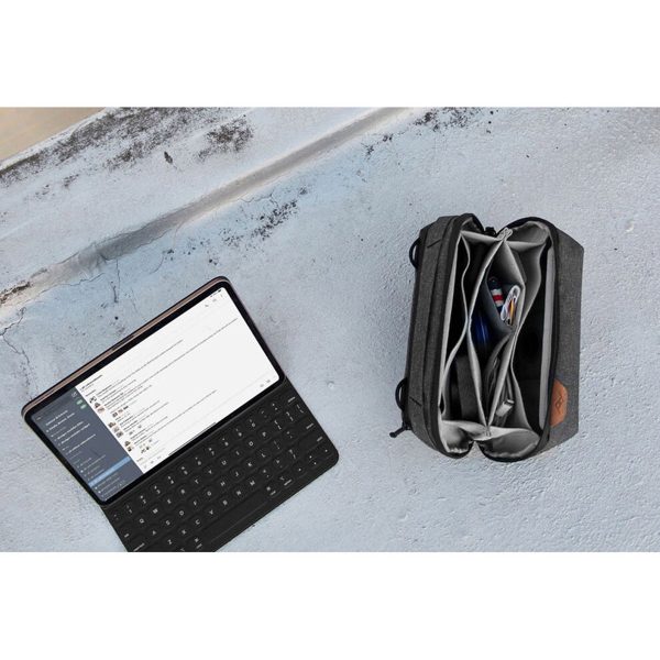Tabletti, jossa on näppäimistö ja jossa näkyy viestisovellus, istuu betonilla avoimen mustan Peak Design Tech Pouch -laukun vieressä, jossa on johtoja, kyniä ja elektroniikkaa.