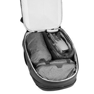 Peak Design Travel Backpack 30L -kamerareppu (musta) on auki, ja siinä näkyy siististi järjestettyjä osioita, joiden sisällä on pakattuja esineitä - rullattu takki tai pussi, drone ja toinen vetoketjullinen lokero.