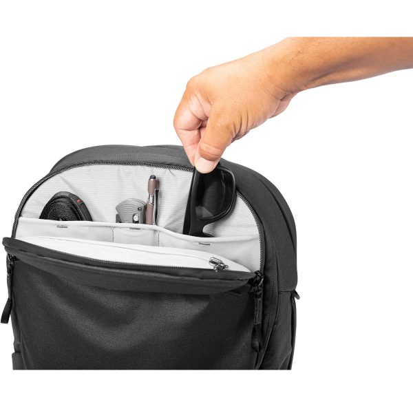Käsi asettaa mustat aurinkolasit Peak Design Travel Backpack 30L -kamerareppu, musta, jonka taskuihin on järjestetty siististi erilaisia tavaroita.