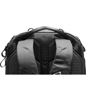 Lähikuva Peak Design Travel Backpack 45L -kamerareppu, musta, jossa korostuvat sen pehmustetut olkahihnat, tukeva kahva ja geometrinen logo takapaneelissa valkoista taustaa vasten.