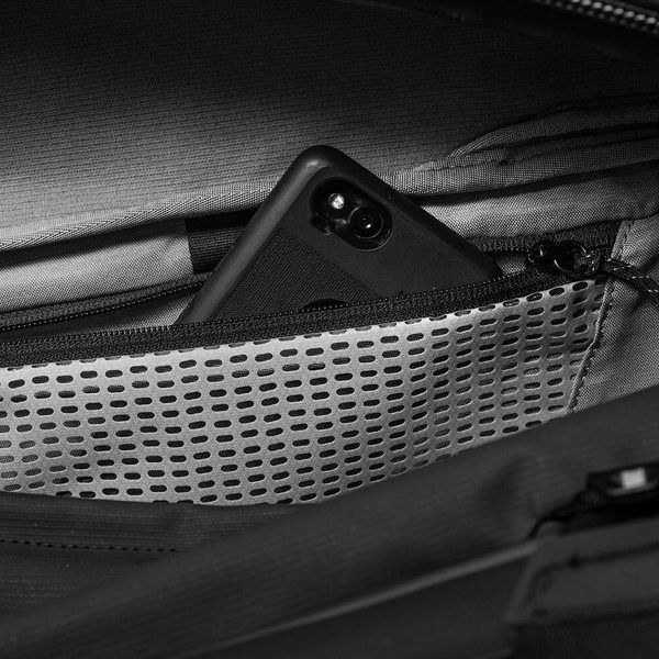 Musta älypuhelin on osittain piilotettu vetoketjullisen verkkotaskun sisään Peak Design Travel Duffel 65L - Black.