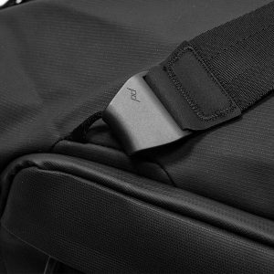 Lähikuva Peak Design Travel Duffel 65L -matkakassista, musta, jossa on pehmustettu olkahihna, muovisolki, jossa on pd-kaiverrus, ja jossa näkyy sen kuvioitu, kestävä materiaali ja tukeva rakenne.