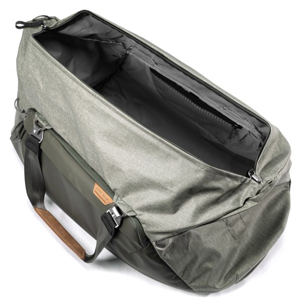 Peak Design Travel Duffel 65L - Sage on tilava, avoin harmaan ja vihreän värinen laukku, jossa on mustat hihnat, ruskea nahkakahva-aksentti ja tyhjä päälokero kuvattuna ylhäältä katsottuna.