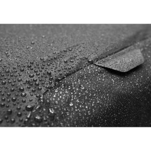Lähikuva vesipisaroista Peak Design Rain Flyn kuvioidulla, tummalla pinnalla, joka korostaa sen vedenkestäviä ominaisuuksia.