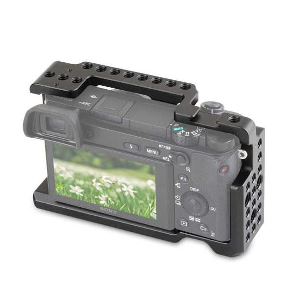 SmallRig 1661 Cage for Sony A6000/A6300/A6500 kätkee sisäänsä digitaalikameran, jonka näytöllä näkyy valkoisia kukkia ja vihreää ruohoa. Mustassa häkissä on useita kiinnitysreikiä yläosassa ja sivuilla.