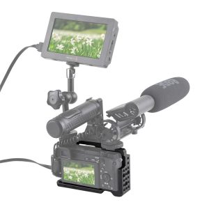 SmallRig 1661 Cage -laitteessa oleva Sony A6000 on varustettu ulkoisella mikrofonilla ja monitorilla, ja siinä näkyy lähikuva valkoisista kukista ja ruohosta. Asetelmassa käytetään kaapeleita liitäntöinä ja se on asennettu tukevaan metallitelineeseen.