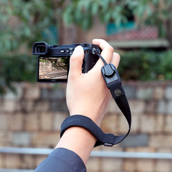 Henkilö käyttää SmallRig 2398 Wrist Strap for Camera -rannehihnaa pitämään digitaalikameraa ja ottaa kuvan kivimuurista ja kameran näytöllä näkyvästä vehreästä maisemasta, jonka tausta on sumea.
