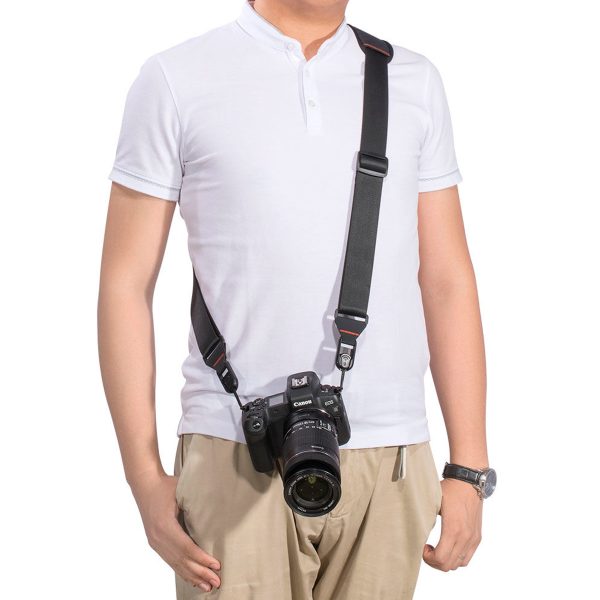The subject is wearing a white short-sleeved polo shirt and beige trousers, and a black camera hangs from his shoulder to his hip via a SmallRig 2428 Camera Shoulder Strap. His left arm rests next to him.