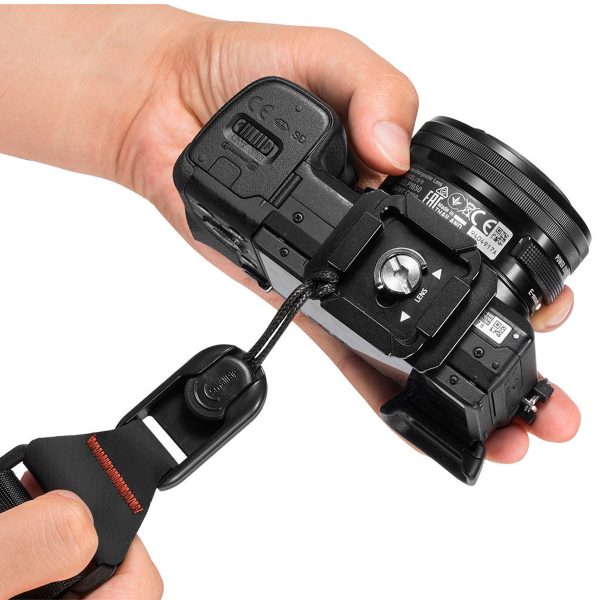 A person attaches a black digital camera to the SmallRig 2428 Camera Shoulder Strap using a mounting plate and screw, holding the camera securely in both hands.