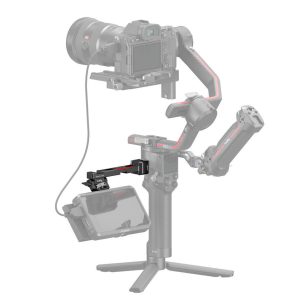 The picture shows a professional camera with a handheld gimbal and tripod on which an external monitor is mounted using the SmallRig 3026B Monitor Mount for DJI Ronin. Some parts of the mount appear semi-transparent grey.