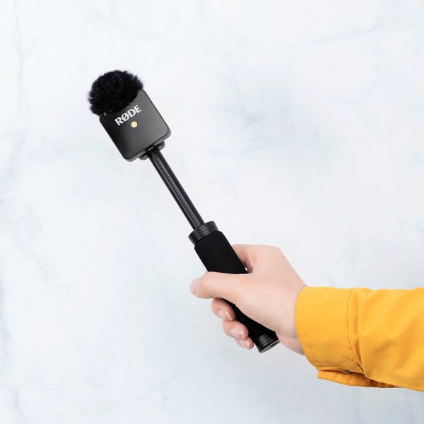 A hand on a yellow sleeve holds a SmallRig 3182 Rode Wireless Go Handheld interviewer with a black foam windscreen and short handle, on a light marble background.