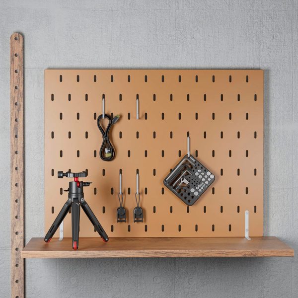 SmallRig-3184-6 A brown SmallRig 3184 Screw & Hex Key Storage Plate with coiled cable, two black adapters and hex keys is mounted on the light grey wall. A small tripod rests on a wooden shelf below.