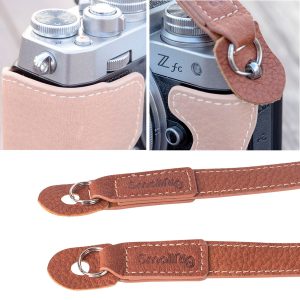 Lähikuva SmallRig 3485 Leather Camera Neck Strap -kamerahihna -kamerahihnan ruskeasta väristä, kiinnitettynä hopeiseen kameraan, jossa on kohokuvioitu tuotemerkki, yksityiskohtaiset ompeleet ja tukevat metalliset rengasliittimet.