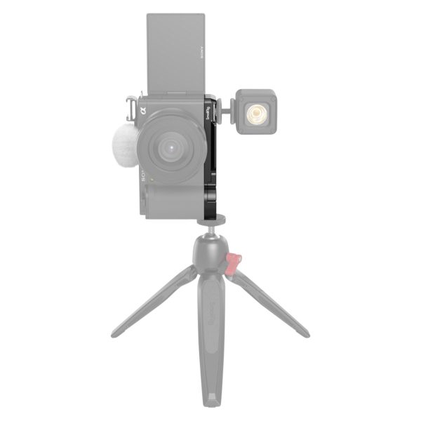 Edestä katsottuna SmallRig 3523 Extension Grip for Sony ZV-E10, musta, kiinnitettynä pienellä jalustalla, ulkoinen valo kameran sivulla ja pystysuoraan asetettu kääntyvä näyttö; kamera ja jalusta näkyvät puoliksi läpinäkyvinä.