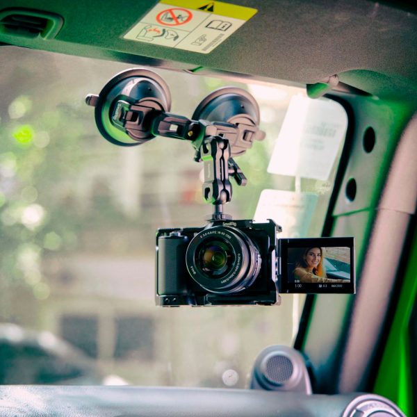 SmallRig 3566 Portable Dual Suction Cup with Camera Mount SC-2K on kiinnitetty auton tuulilasiin ja tallentaa videon naisesta, jota näytetään sen ulos käännettävällä näytöllä, kun auton sisäkatto ja varoitustarrat näkyvät ja tausta on sumea.