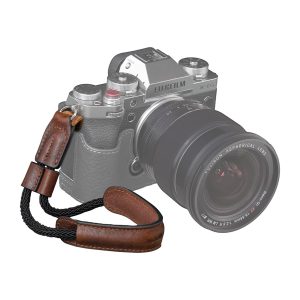SmallRig 3926 Universal Wrist Strap Vintage -rannehihna, ruskeaa nahkaa ja mustaa punosta, on esillä osittain haalistuneen Fujifilm X-T5 -kameran edessä, jossa on suuri objektiivi, joka korostaa tyylikästä rannehihnaa.