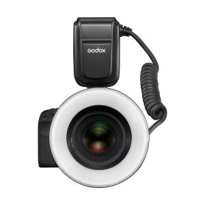 Mustan värinen Godox MF-R76C TTL Macro Ring Flash - Canon on kiinnitetty kameran objektiivin etupuolelle ylhäältä kuvattuna. Pyöreä salama ympäröi objektiivia, ja sen virtalähde on kytketty sen päällä olevalla kierrekaapelilla.