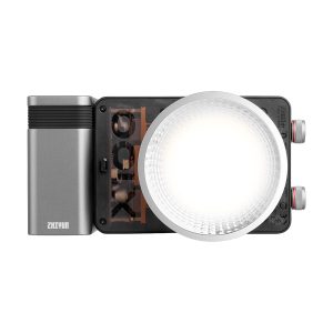 Zhiyun LED Molus X100 COB Light Pro on kompakti, suorakulmainen LED-videovalaisin, jossa on suuri pyöreä diffuusori, metallinharmaa akkupaketti vasemmalla puolella Zhiyunin tuotemerkillä ja säätöpyörät oikealla puolella.