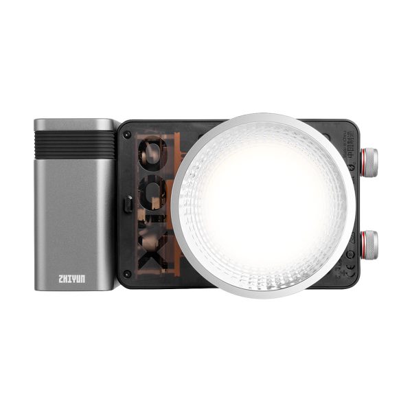 Zhiyun LED Molus X100 COB Light Pro on kompakti, suorakulmainen LED-videovalaisin, jossa on suuri pyöreä diffuusori, metallinharmaa akkupaketti vasemmalla puolella Zhiyunin tuotemerkillä ja säätöpyörät oikealla puolella.