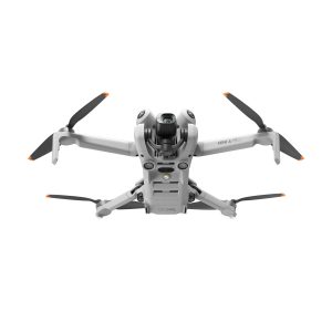 Hopeanvärinen DJI Mini 4 Pro -lennokki, jossa on neljä oranssilla kärjellä varustettua potkuria ja etukamera, näkyy lennossa valkoista taustaa vasten.