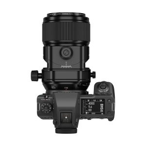 Ylhäältä katsottuna Fujifilm Fujinon GF 110mm f/5.6 T/S -objektiivi kiinnitettynä digitaalikameraan, jossa näyttö ja säätimet näyttävät ISO-, aukko- ja suljinaika-asetukset tavallista valkoista taustaa vasten.