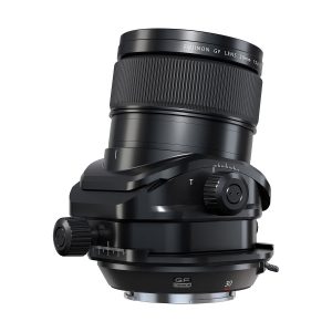Fujifilm Fujinon GF 30mm f/5.6 T/S -objektiivi mustana, jossa on säätönupit ja tilt-shift-mekanismi, kuvattuna kulmassa valkoisella taustalla.