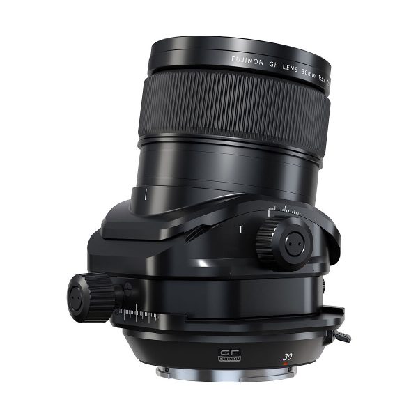 Fujifilm Fujinon GF 30mm f/5.6 T/S -objektiivi mustana, jossa on säätönupit ja tilt-shift-mekanismi, kuvattuna kulmassa valkoisella taustalla.