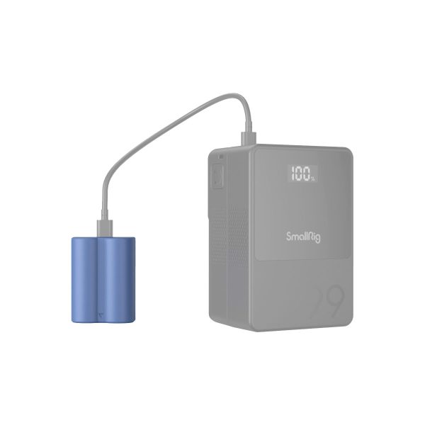 Sininen akku on liitetty kaapelilla harmaaseen SmallRig 4266 USB-C ladattavaan kamera-akkuun NP-W235, jonka digitaalisessa näytössä lukee "100L". Virtapankki on suorakulmainen ja siinä on kuvioitu pinta.