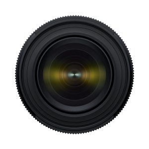 Tamron_17-50_f4_004 Lähikuva Tamron 17-50mm F/4 Di III VXD -objektiivista Sony E:lle, jossa objektiivi on suunnattu eteenpäin, ja siinä on näkyvät samankeskiset renkaat ja heijastetut lasielementit valkoista taustaa vasten.