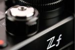 Lähikuva Nikon Zf -järjestelmäkamerasta, musta, keskittyen "Zf"-logoon ja metalliseen säätöpyörään, jossa on yksityiskohtaisia kuvioita.