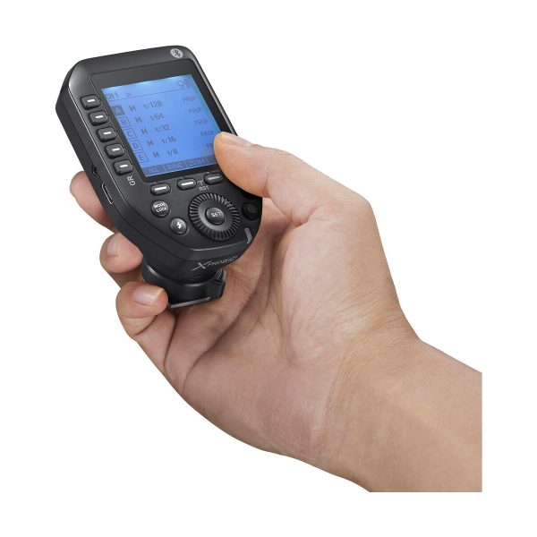 In hand is the Godox XPro II transmitter for Fujifilm, a black device with a settings display and several buttons designed to control the camera's flash.